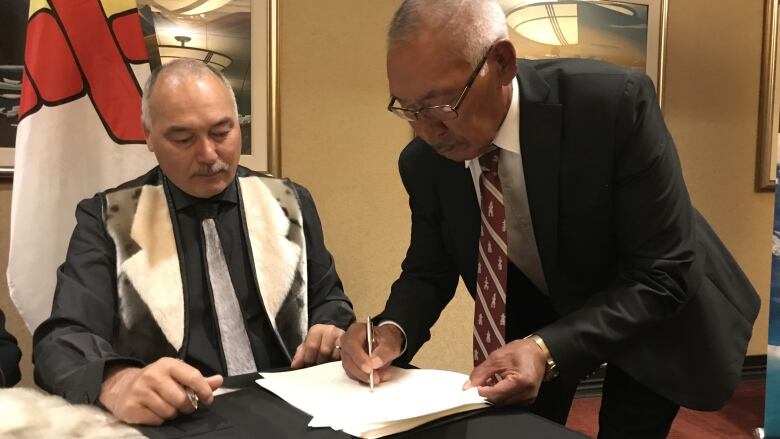 Two men signing a document at a desk.