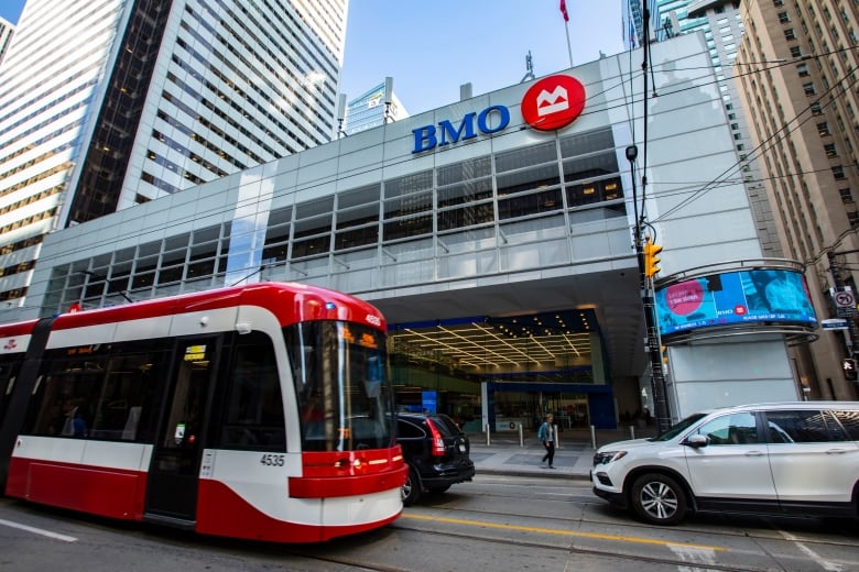 A streetcar and other city traffic pass in front of a large building bearing the Bank of Montreal logo. 