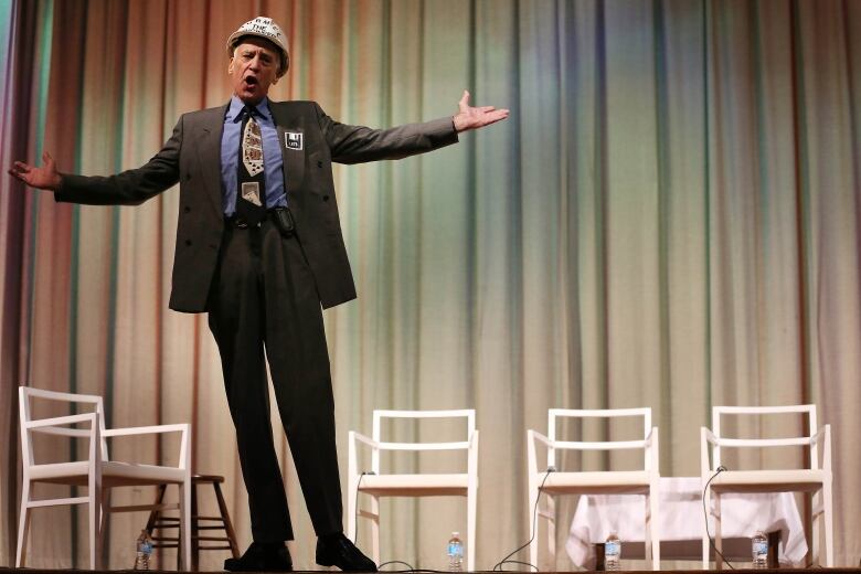 A person stands on stage surrounded by empty white chairs