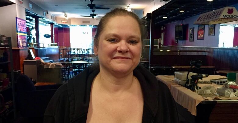 A woman wearing a sweater with an empty pub behind her.