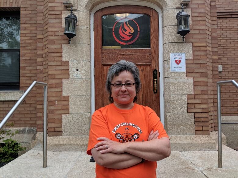 Woman with short hair and glasses wears an orange shirt.