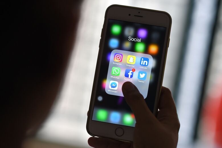 A person holds a phone with a variety of social media apps displayed.