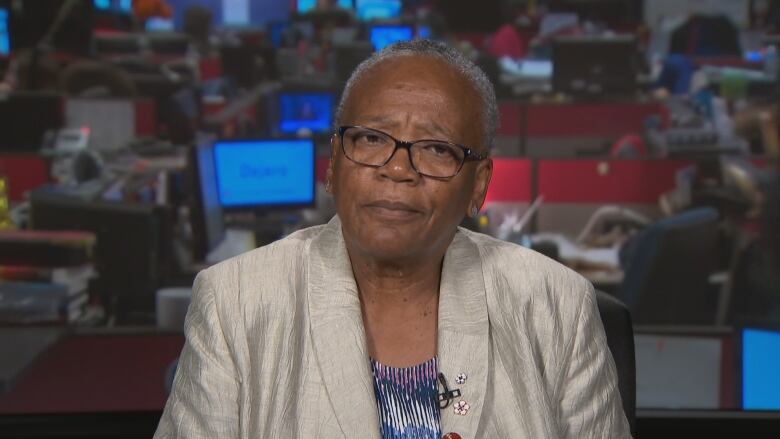 A Black woman wearing glasses and a metallic beige blazer