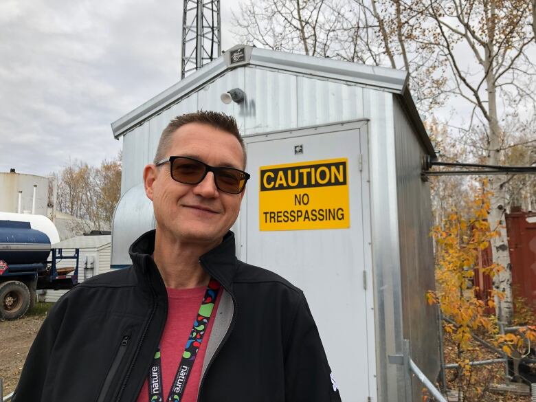 A man stands near a shed.