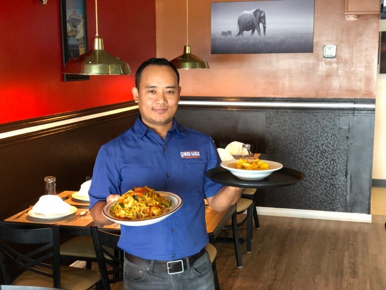 A man holding two heaping platters of food in a restaurant.