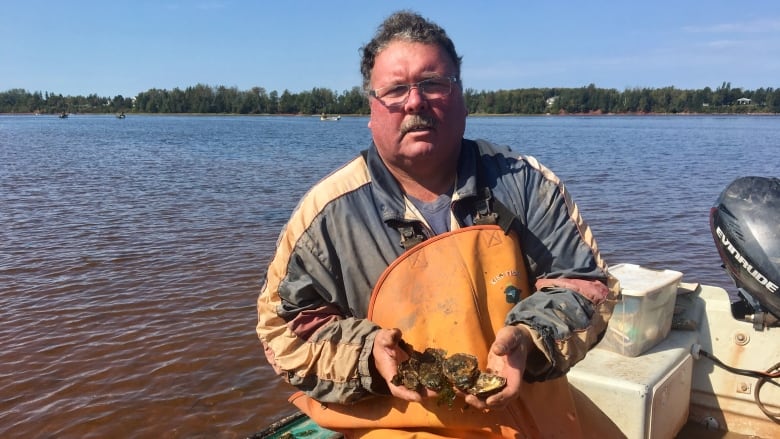 Bob MacLeod, in his fishing boat, holds a handful of oysters.