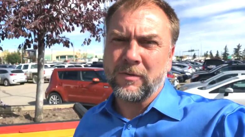 A man in a blue shirt appears to be recording himself in a parking lot.