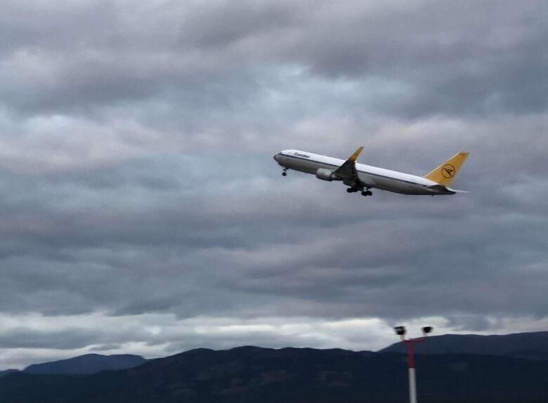 A passenger jet is seen taking off, with mountains in the background.