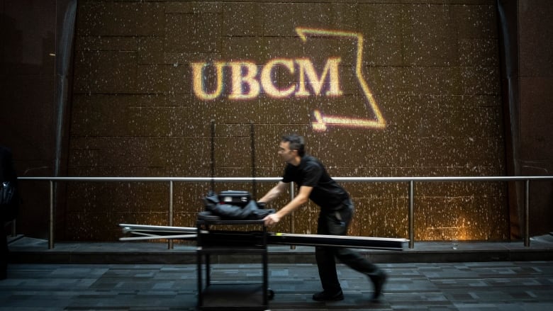 A man pushes a cart past a sign that reads 'UBCM'.