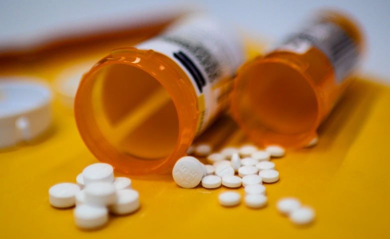 Two plastic bottles of pills shown spilling contents out on a table, close up. 