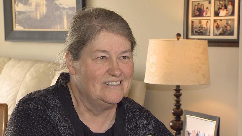 Mary Noye in home with family pictures on wall in the background.