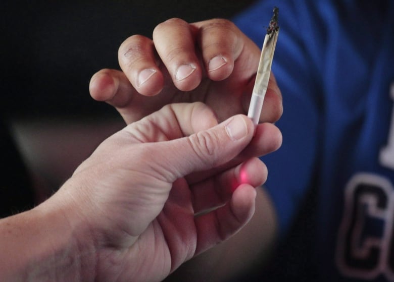 A hand handing a marijuana joint to another hand.