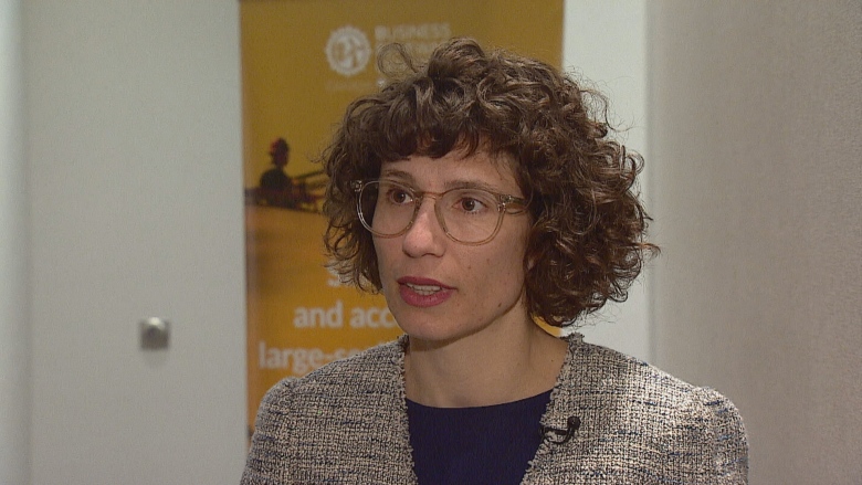 A woman with short brown curly hair wears glasses.