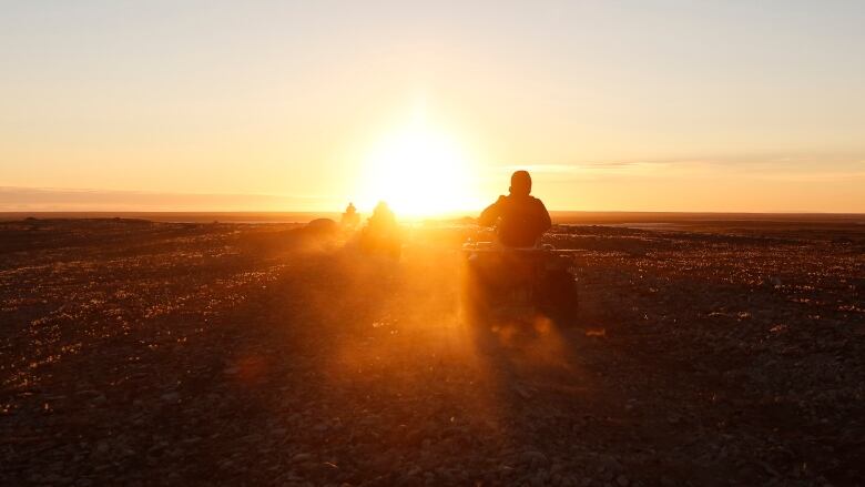 A silhouette of a person driving a vehicle is seen against an orange sunrise sky.