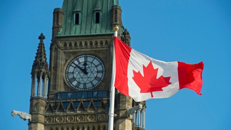 A clock tower with a Canadian flag waving.