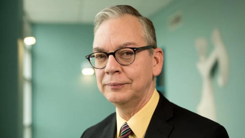 A man in horn-rimmed glasses stares into the camera.