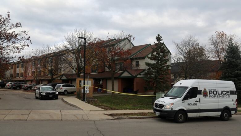 A row of townhouses is surrounded by police tape and has police vehicles parked outside.