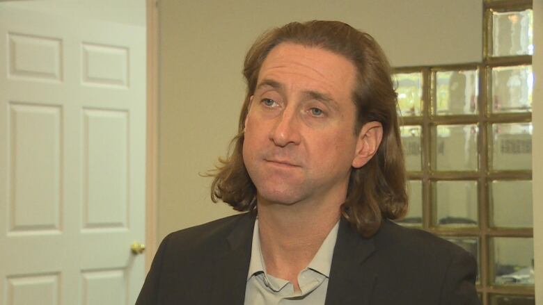 A man with long brown hair wearing a suit.