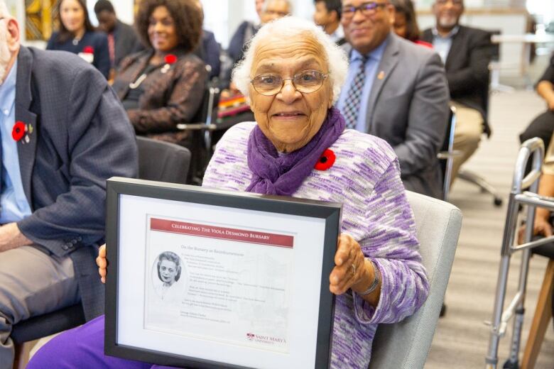 A older Black woman holds a plaque that reads 