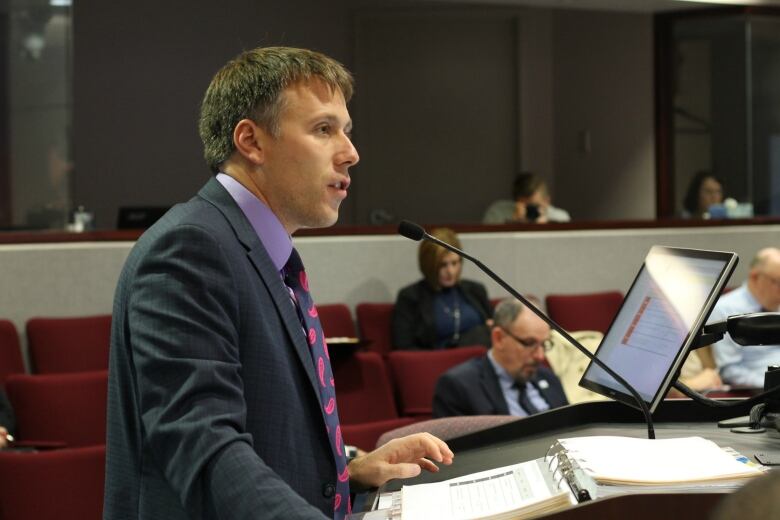 A man in a dark coloured suit standing at a podium speaking. 