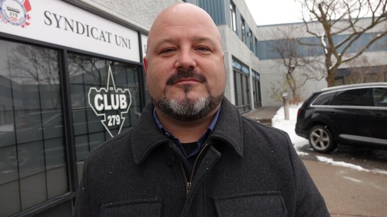 A man with a goatee stands outside of an office building