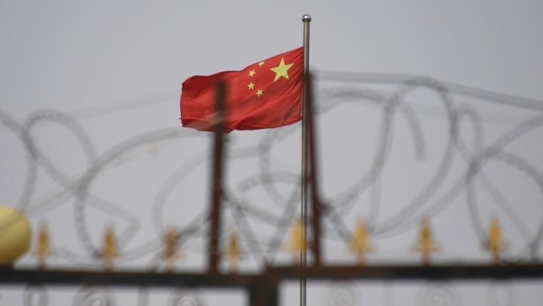 A Chinese flag is seen behind a fence topped with razor wire.