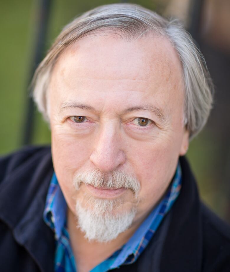 An old white man with grey hair and a goatee is seen in a wearing a navy button up weater