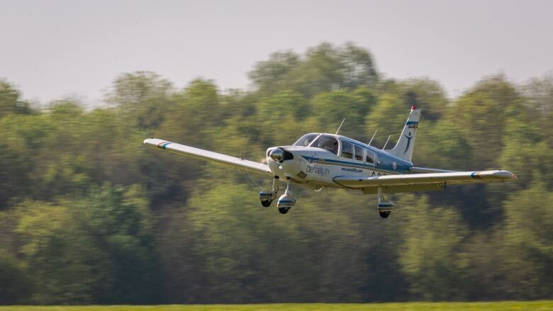 A small plane flies, with a motion blur on the trees in the background. 