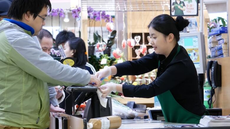 A woman at a cashier counter rings a customer through. 