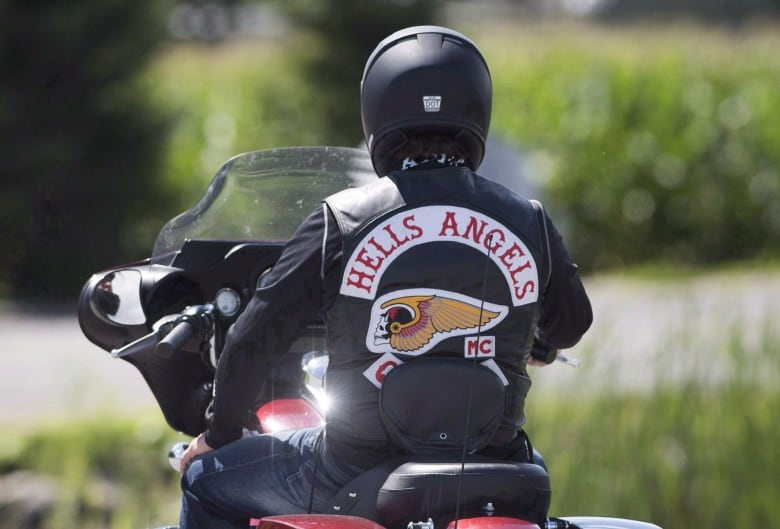 A person in a Hells Angels leather jacket rides a motorcycle 