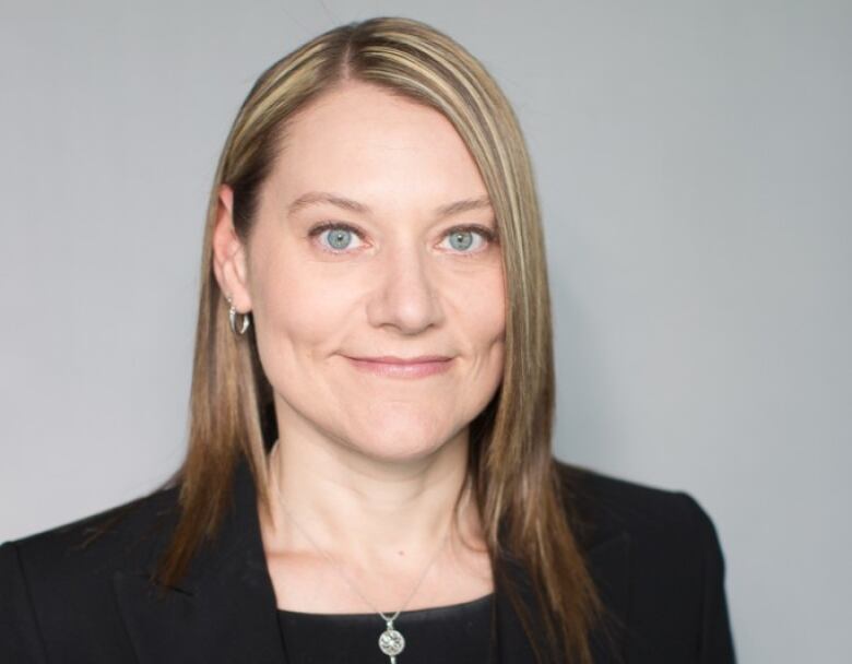 A woman with shoulder-length blond hair and a black blazer smiles while looking into the camera.