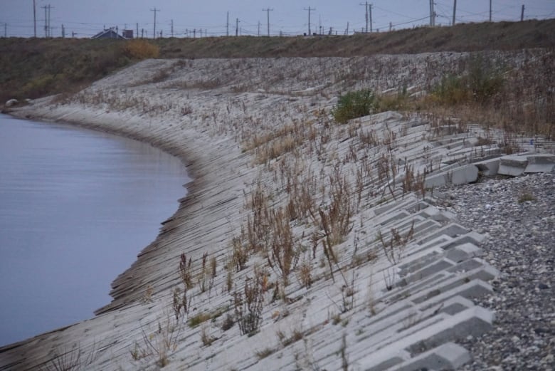 A dike made of gravel and bricks curves around with water on one side and the tops of hydro poles on the other 