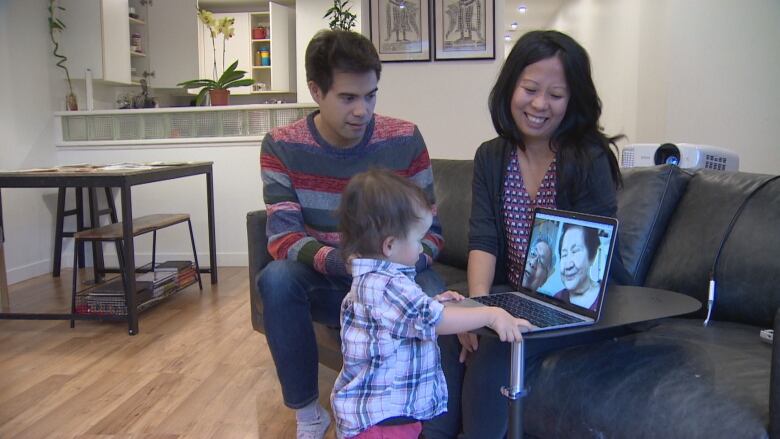 An infant looks at family on a computer screen while the parents look on