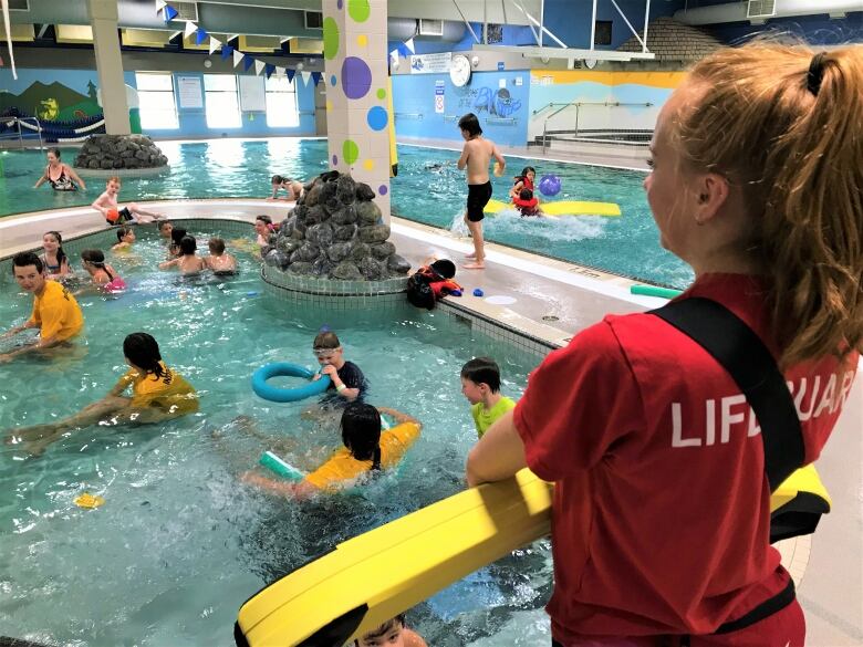 A lifeguard stands over an indoor pool filled with children.