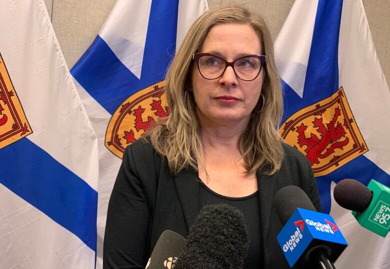 A woman in a black outfit looks at the camera in front of Nova Scotia flags. 