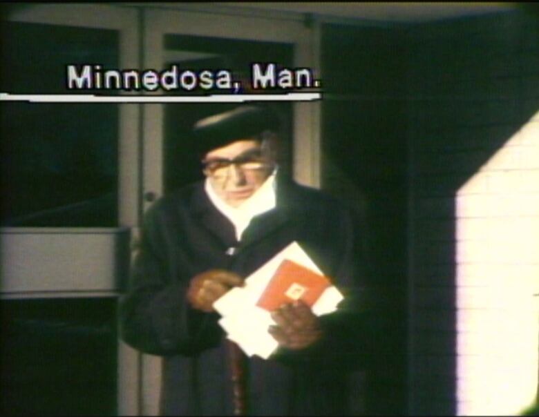 Man in winter coat and hat exiting building with armful of mail