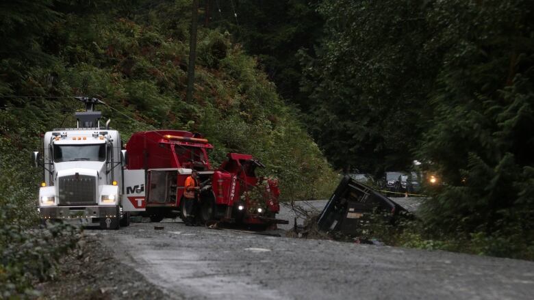 A tow truck pulls a crashed bus from an embankment it fell off on a dirt road.