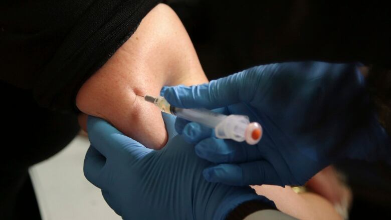 A closeup shows a person getting a needle in their arm.