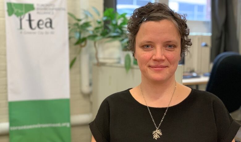 Emily Alfred looks at the camera. Behind her, to the left, is a green and white Toronto Environmental Alliance sign. 