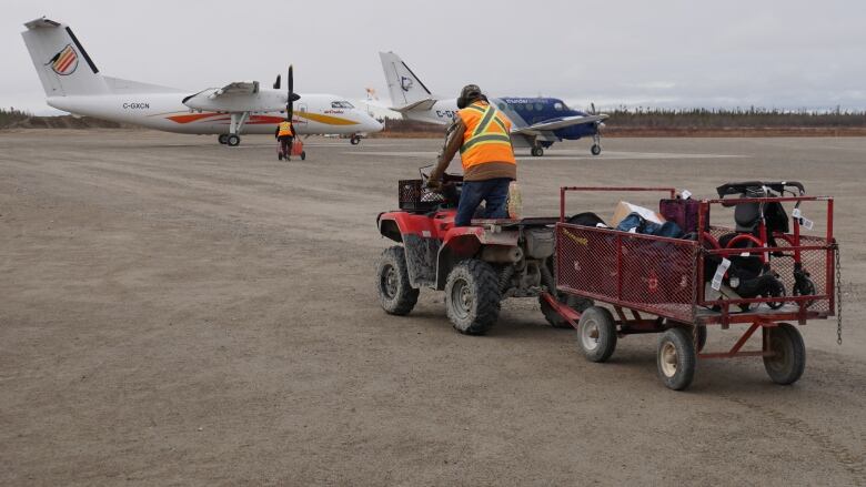 An ATV pulls a cart full of baggage across a runway toward two airplanes