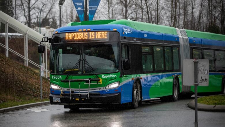 A green bus drives through a rainy street, with the words 'Rapidbus is here' on its chyron.