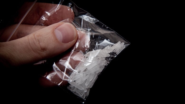 A hand holds a small baggy containing shards of clear crystal meth.