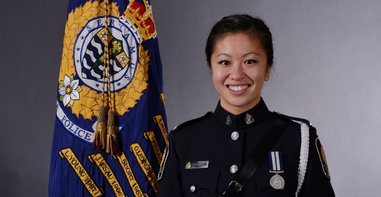 A woman in a police uniform smiles as she stands next to a flag of the Vancouver Police Department.