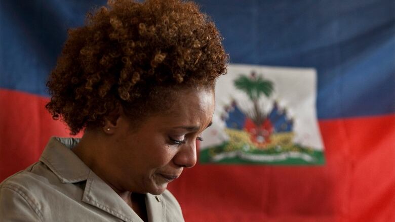 Woman with a sad expression on her face and standing in front of the flag of Haiti looks down