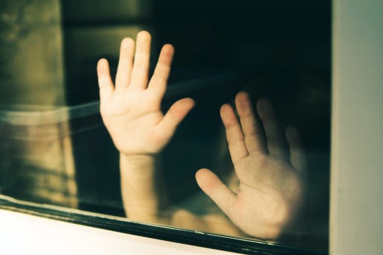 A child's hands are seen pressed up against a window.