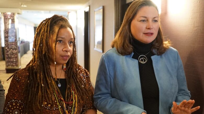 Two women standing side-by-side answering questions by the media