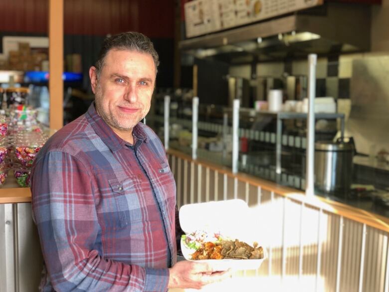 A man holds a styrofoam container of food by a food counter.