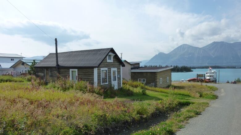 Small house on a road leading down to a large lake with mountains in the background.