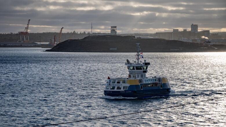 A blue, white and yellow ferry crosses the harbour with a small island and the port in the background