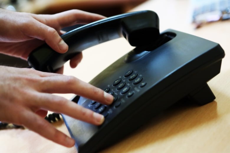 A closeup shows a hand dialling numbers on a landline phone.